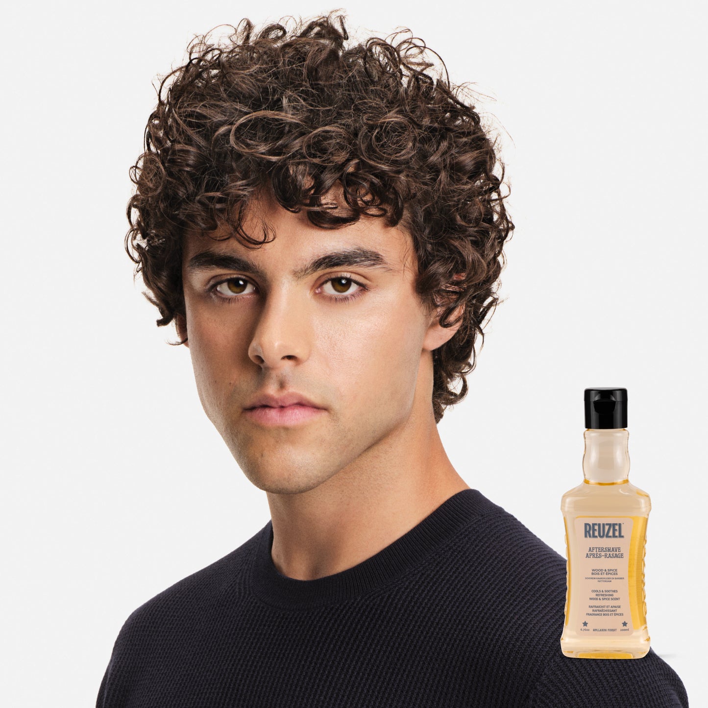 Man with styled hair next to a bottle of Reuzel Aftershave on a white background