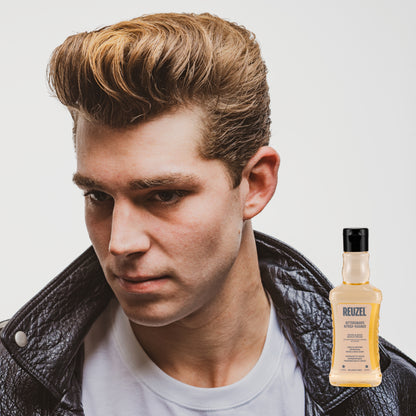 Man with styled hair wearing a leather jacket, with a bottle of Reuzel Aftershave