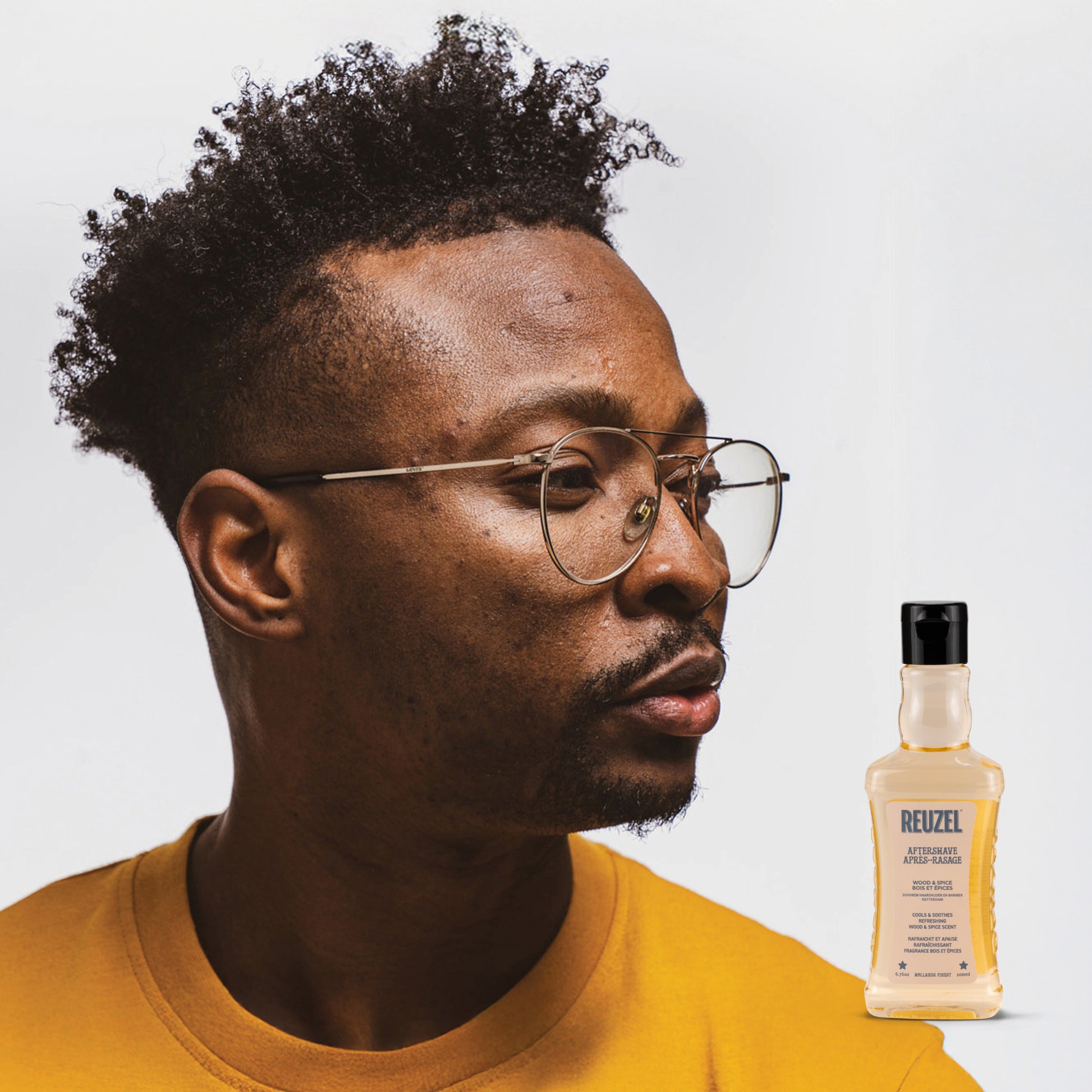 Man wearing glasses with a bottle of Reuzel Aftershave on a light gray background