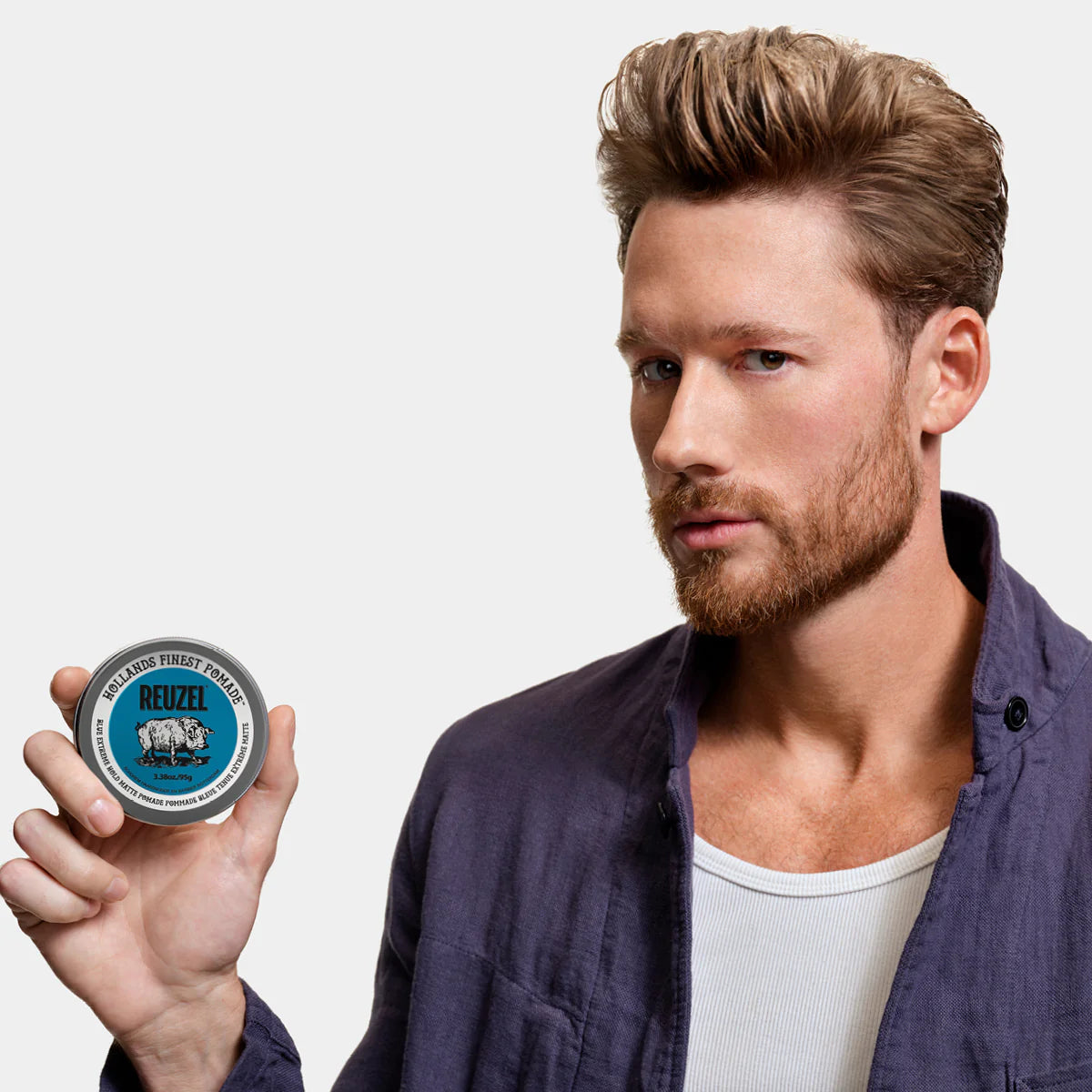 Man holding a container of Reuzel Blue Extreme Pomade against a plain background