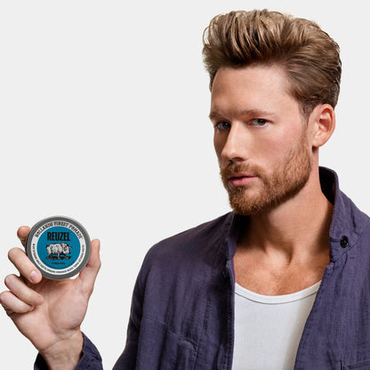 Man holding a container of Reuzel Blue Extreme Pomade against a plain background
